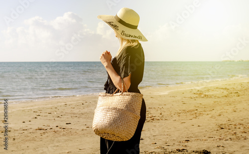 Young blonde women with straw hat holding a basket in his hand and looking at sea . Greece summer vacation .