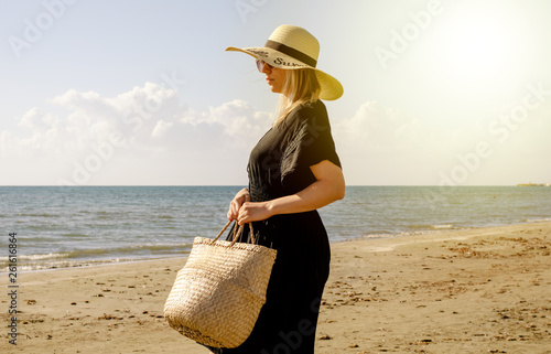 Young blonde women  with straw hat   holding  a  basket in his handand and  looking for a place on the beach to settle down  . Greece summer vacation . photo