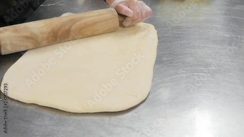 woman presses out dough with wood rolling pin. Woman uses wooden rolling pin to flatten dough.