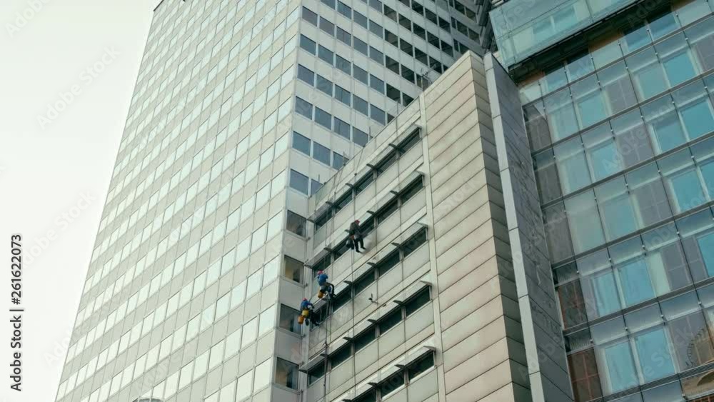 Extreme Long Shot of Three Window Washers Men Working and Cleaning Glass Windows on Modern Office Building Outside in Spring. 4K Slow Motion Static and then Panning Shot Extreme Long Shot of Three Window Washers Men Working and Cleaning Glass Windows on Modern Office Building Outside in Spring. 4K Slow Motion Static and then Panning Shot