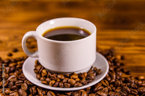 Cup of hot coffee and scattered coffee beans on wooden table