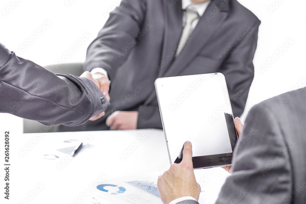 businessman with a digital tablet on the background of a handshake of business partners businessman with a digital tablet on the background of a handshake of business partners