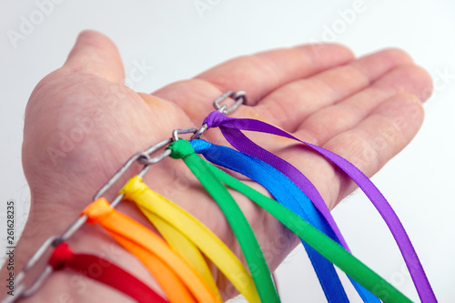 LGBT pride flag, built of colored ribbons tied on an iron chain in the hand of a man, short focus, on a white background