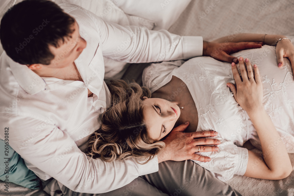 husband hugs his pregnant wife while sitting on the bed. husband hugs his pregnant wife while sitting on the bed.