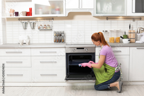 Woman cleaning oven tray with rag in kitchen