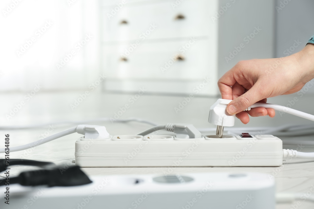 Woman inserting power plug into extension cord on floor indoors, closeup with space for text. Electrician's professional equipment Woman inserting power plug into extension cord on floor indoors, closeup with space for text. Electrician's professional equipment