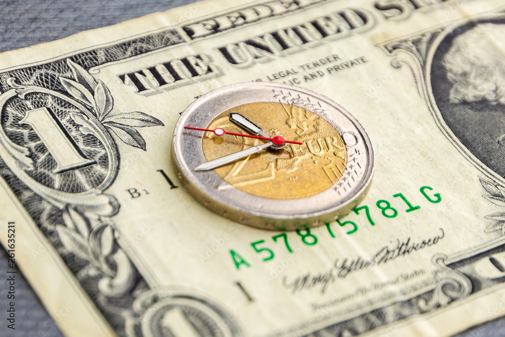 currency exchange rate control: 2 euro coin with hour hands on 1 dollar bill, short focus, close currency exchange rate control: 2 euro coin with hour hands on 1 dollar bill, short focus, close
