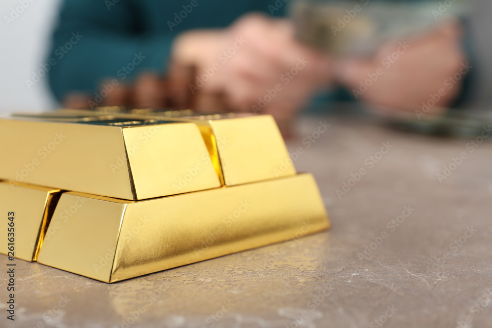 Stacked gold bars and man counting money at table, closeup. Space for text Stacked gold bars and man counting money at table, closeup. Space for text