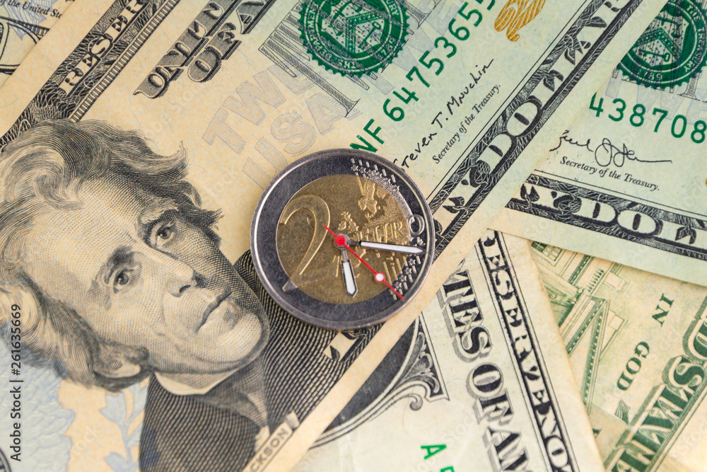 exchange rate: 2 euro coin with hour hands on a pile of dollars, short focus, close exchange rate: 2 euro coin with hour hands on a pile of dollars, short focus, close