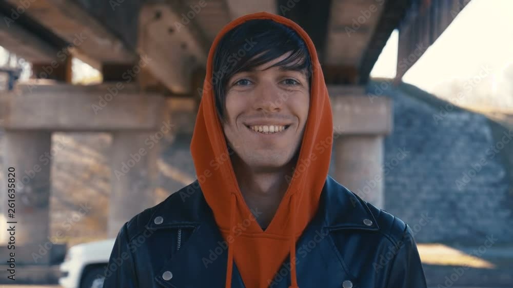 Portrait of happy cute caucasian man in red hoodie smiling in city at urban background Portrait of happy cute caucasian man in red hoodie smiling in city at urban background