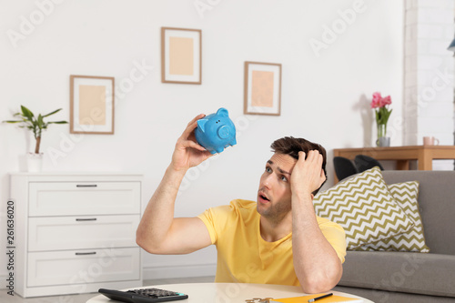 Foto Sad man looking for money in piggy bank at table indoors
