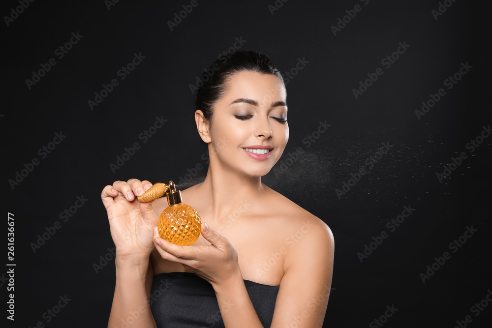 Young woman spraying perfume on black background Young woman spraying perfume on black background