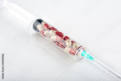 Syringe filled with red pills on white background