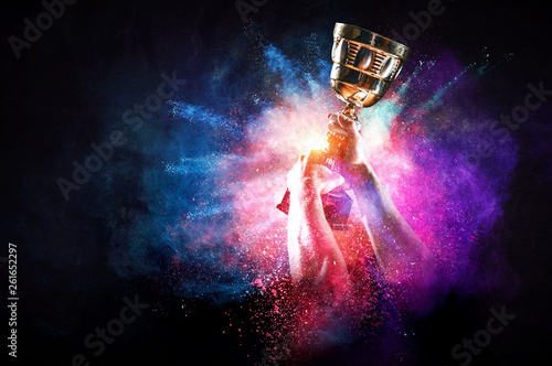 Photographie Hands holding champion cup on colourful splashes background