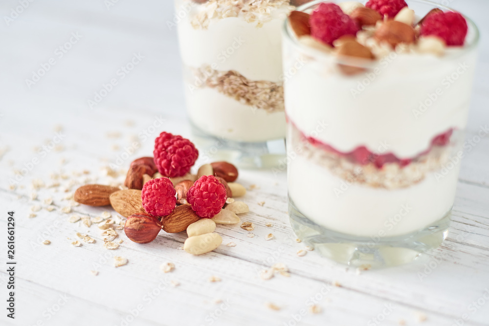 Two glasses of greek yogurt granola with raspberries, oatmeal flakes and nuts on a white background. Healthy nutrition Two glasses of greek yogurt granola with raspberries, oatmeal flakes and nuts on a white background. Healthy nutrition
