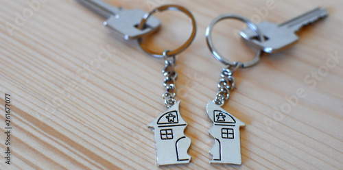 Two keys with splitted or broken key rings with pendant in shape of house divided in two parts on wooden background with copy space. Dividing house when divorce, division of property, real estate heri photo