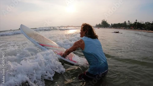 Surfer goes into the ocean with surfboard at Weligama surf spot in Sri Lanka