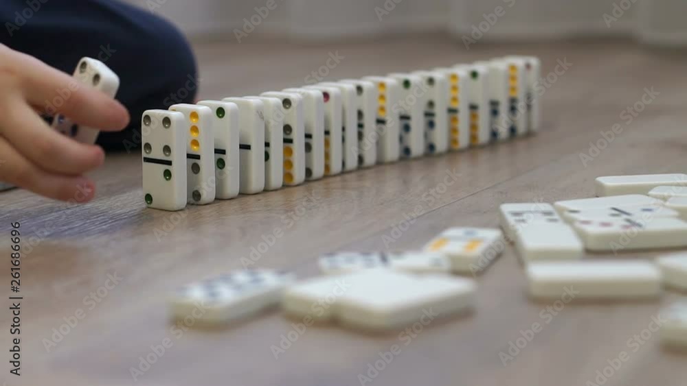 Close-up of a little boy playing with dominoes on the floor of the house, he puts them next to them to alternately fall. The reaction of falling dominoes. Close-up of a little boy playing with dominoes on the floor of the house, he puts them next to them to alternately fall. The reaction of falling dominoes.