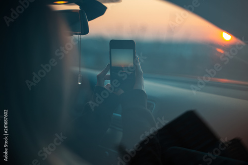 Young girl taking photo of sunset from car.