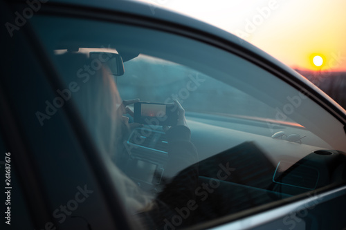 Young girl taking photo of sunset from car.