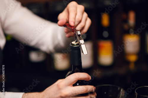 Foto Elegant young sommelier with bow tie uncorking bottle of wine in wine boutique