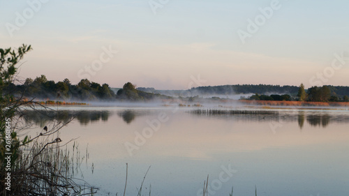 Morning dawn of the sun through the mist over the water. Early morning in the forest on the river. © Payllik