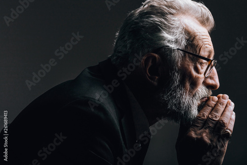 Head portrait of senior caucasion well-groomed businessman in spectacles wearing posing in profile isolated over black background