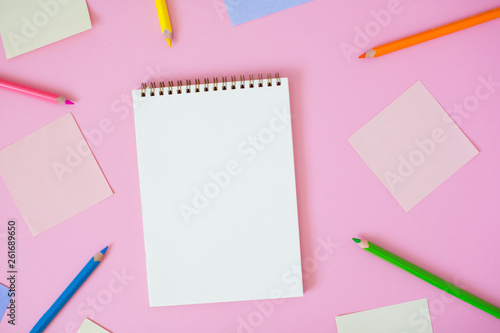 Color note papers and notebook with pencils on pink background.