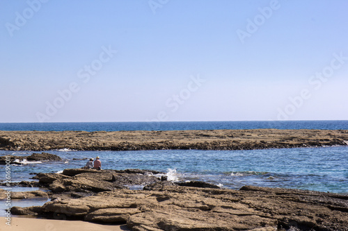 Coastline with sedimentary rocks and tide pools at the northern Cyprus with two persons sitting for sun bathe