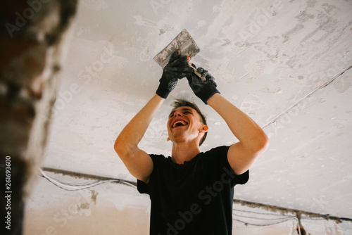 A man removes old paint from the ceiling with a spatula