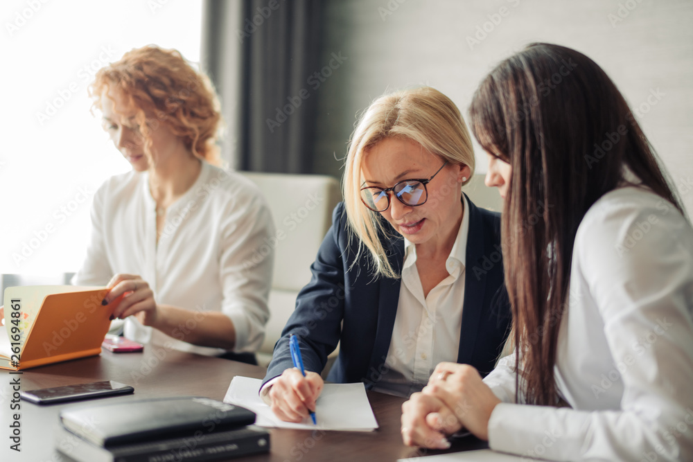 Three focused caucasian young business women with different hairstyle working together, brainstorming in office. Three focused caucasian young business women with different hairstyle working together, brainstorming in office.