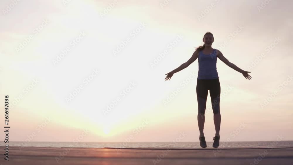 Woman at sunset doing cardio exercises. She jumps up and raises her arms. jumping jack at sunset by the sea. The best slimming workout Woman at sunset doing cardio exercises. She jumps up and raises her arms. jumping jack at sunset by the sea. The best slimming workout