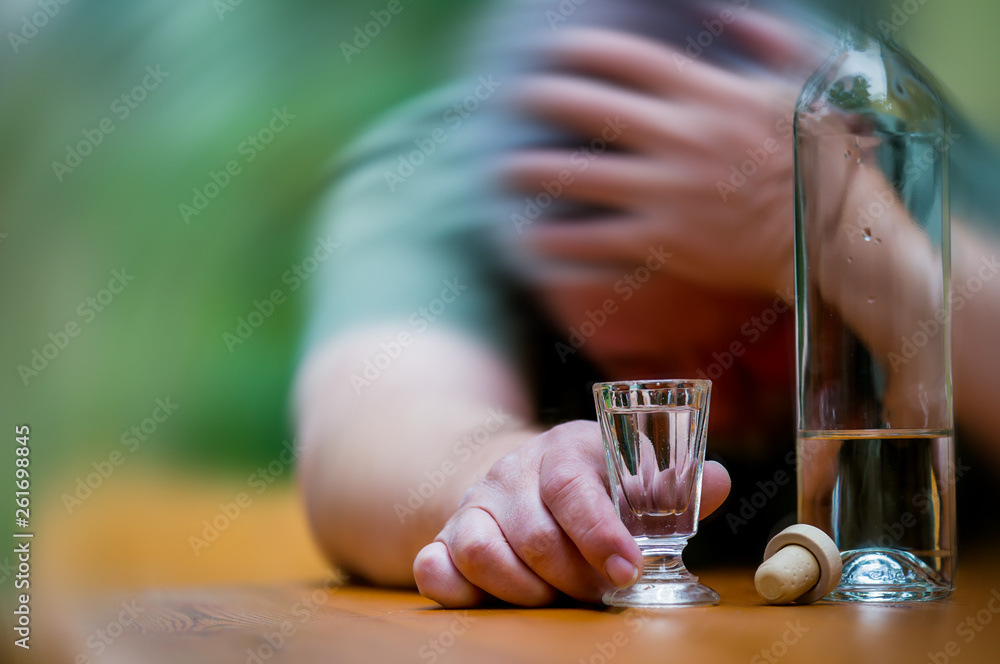 A man sits drunk with a bottle of alcohol at a table. Concept of alcoholism.