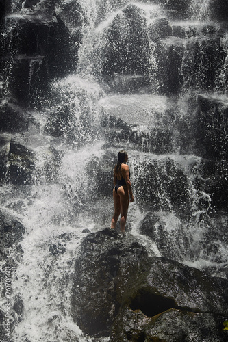 A young girl stands under a waterfall