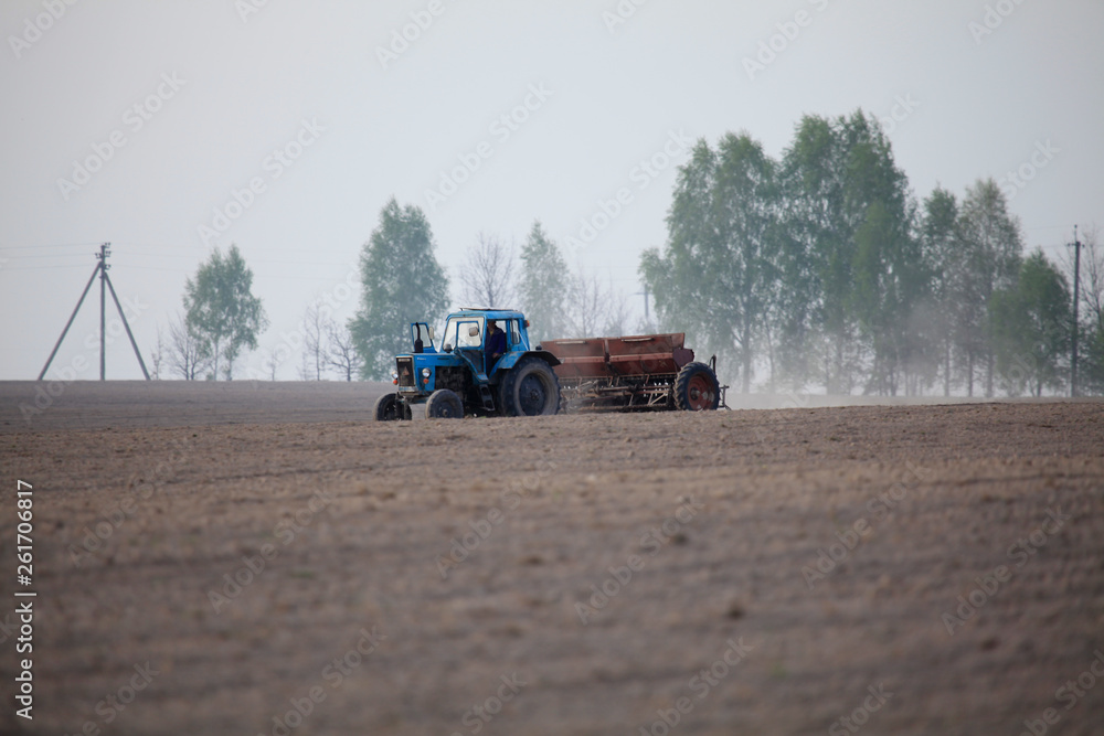 Fototapeta premium Spring agricultural works. Soviet tractor with ancient seeder. Planting cereals. An old sowing seeds machine on the plowed field. Sowing graining