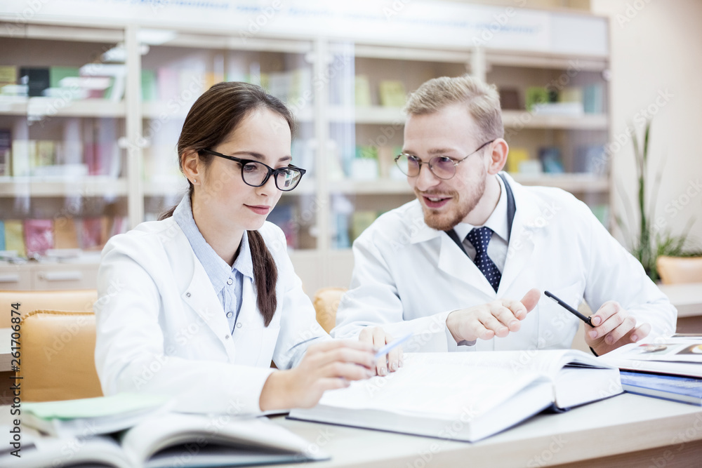 Obraz premium Joyful young general practitioner. Smiling professional doctor in white coat discussing diagnosis in library. Health concept