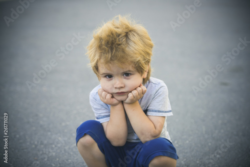 Sad boy looking at the camera. Child alone. One sad little boy sitting on the street. Unhappy child. Think of a new idea.