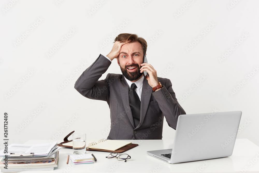 Everything goes wrong, OMG, it's a disaster! Dressed in a suit respectable office worker sitting at desktop grasping his head panics, nervous, is in a difficult situation, holding a phone near his ear Everything goes wrong, OMG, it's a disaster! Dressed in a suit respectable office worker sitting at desktop grasping his head panics, nervous, is in a difficult situation, holding a phone near his ear