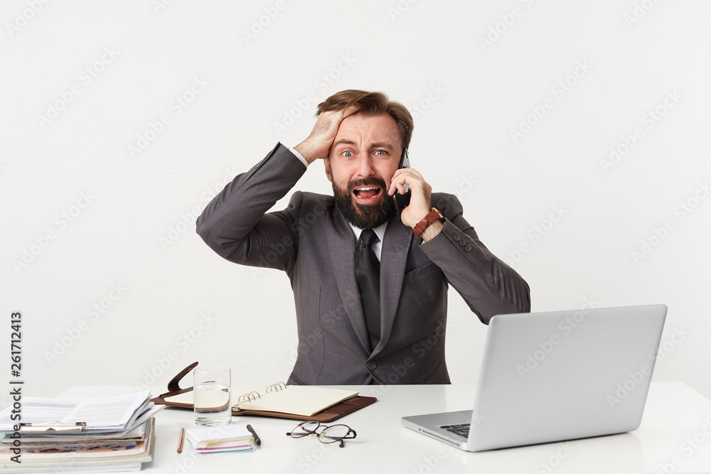 It's a disaster, everything goes wrong, OMG! Respectable office worker sitting at table grasping his head, nervous, is in a difficult situation, holding a phone near his ear, screams from panic It's a disaster, everything goes wrong, OMG! Respectable office worker sitting at table grasping his head, nervous, is in a difficult situation, holding a phone near his ear, screams from panic