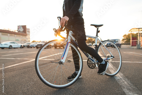 Background. Bicyclist's legs with a white highway bike close-up on the background of the sunset. Rider and a bicycle on the background of the sun and urban landscape. Transport and people.