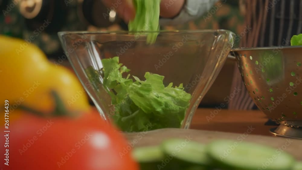 Hands ripping lettuce and putting it in a glass bowl Hands ripping lettuce and putting it in a glass bowl
