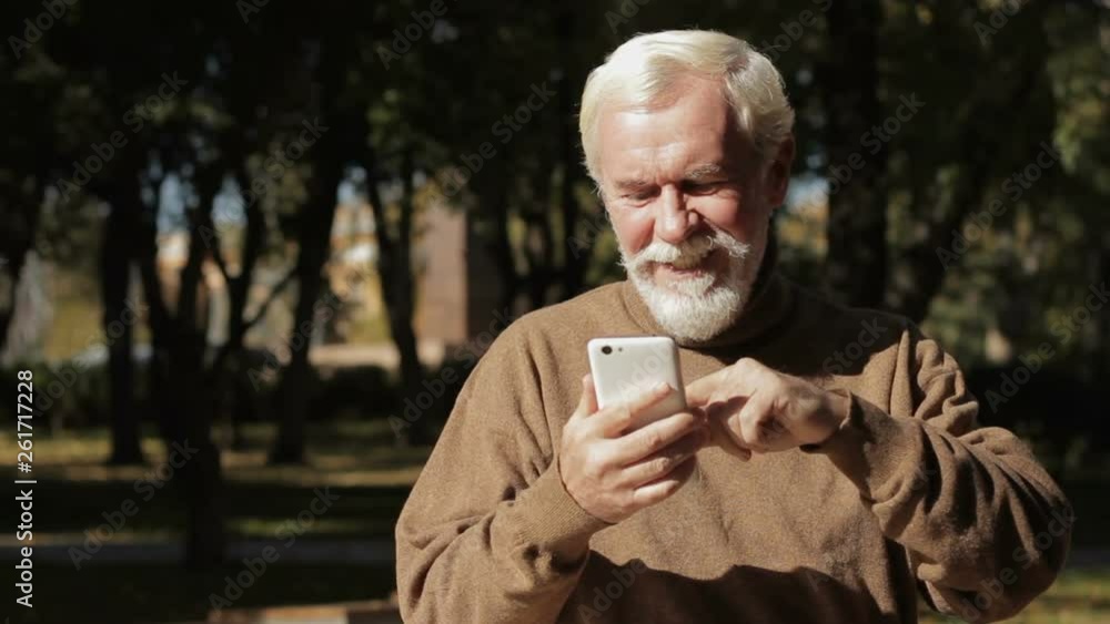 Funny bearded grandpa using smartphone, scrolling news, searching in internet