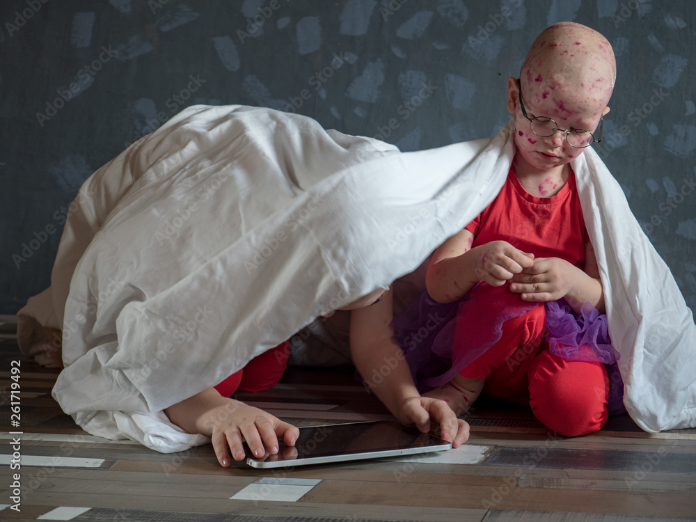 Fototapeta premium Caucasian children in pink t-shirt with smartphone on floor. Boys posing for camera under white blanket. One of children blond in glasses has chicken pox. Mom smeared follicles with pink solution