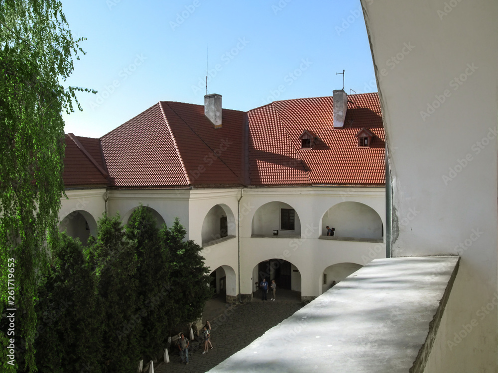 Mukachevo, Ukraine - May 3, 2018: Top view of the courtyard with a white building and greenery in the Castle Palanok. Tourists near the medieval building with arched windows and a red tiled roof
