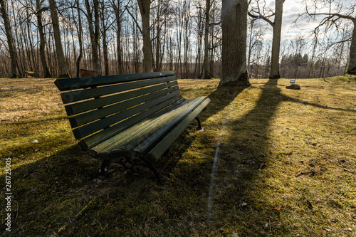 LIEPUPE  LATVIA - APRIL 13  2019  Liepupes Muiza manor in beautiful sunny Spring weather with blue sky and clouds - Beautiful park with tall old trees - Green Bench