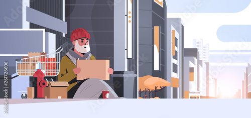 poor man with sitting on floor begging for help beggar guy holding sign board homeless concept modern city street buildings exterior sunset cityscape background horizontal full length