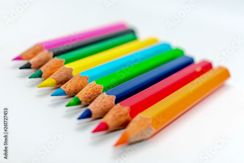 Multi colored bunch of assorted rainbow color pencil line up in a row close together side by side arranged in white background, flat lay. Selective focus blur image. Back to school creative concept