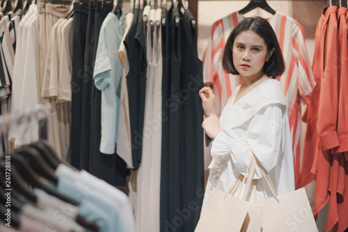Young Asian beautiful woman shot hair shopping buying clothes in a shopping mall store. Woman standing to finding a new clothes which hanging.