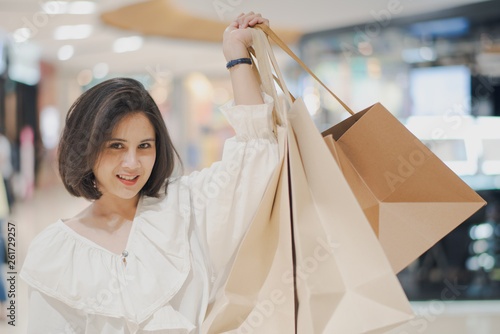 Young Asian beautiful woman shot hair smiling to shopping in a shopping mall. Woman standing and holding which show a shopping bag in the store.