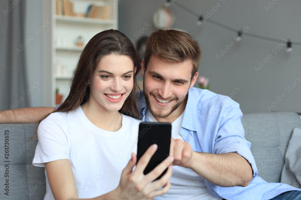 Young couple watching online content in a smart phone sitting on a sofa at home in the living room. Young couple watching online content in a smart phone sitting on a sofa at home in the living room.